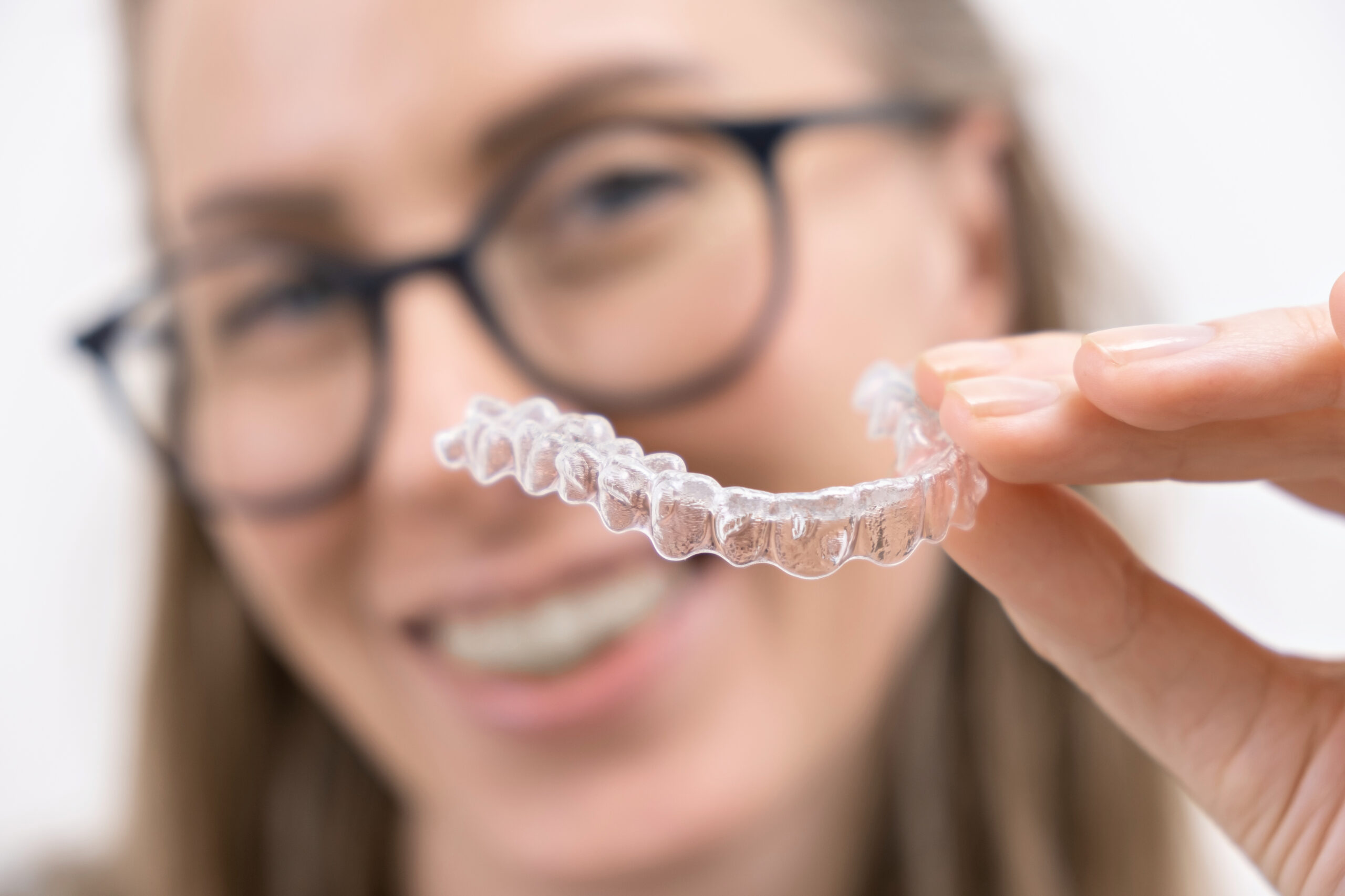 Smiling woman holding affordable clear aligners, highlighting a cost-effective and discreet orthodontic solution for straighter teeth.