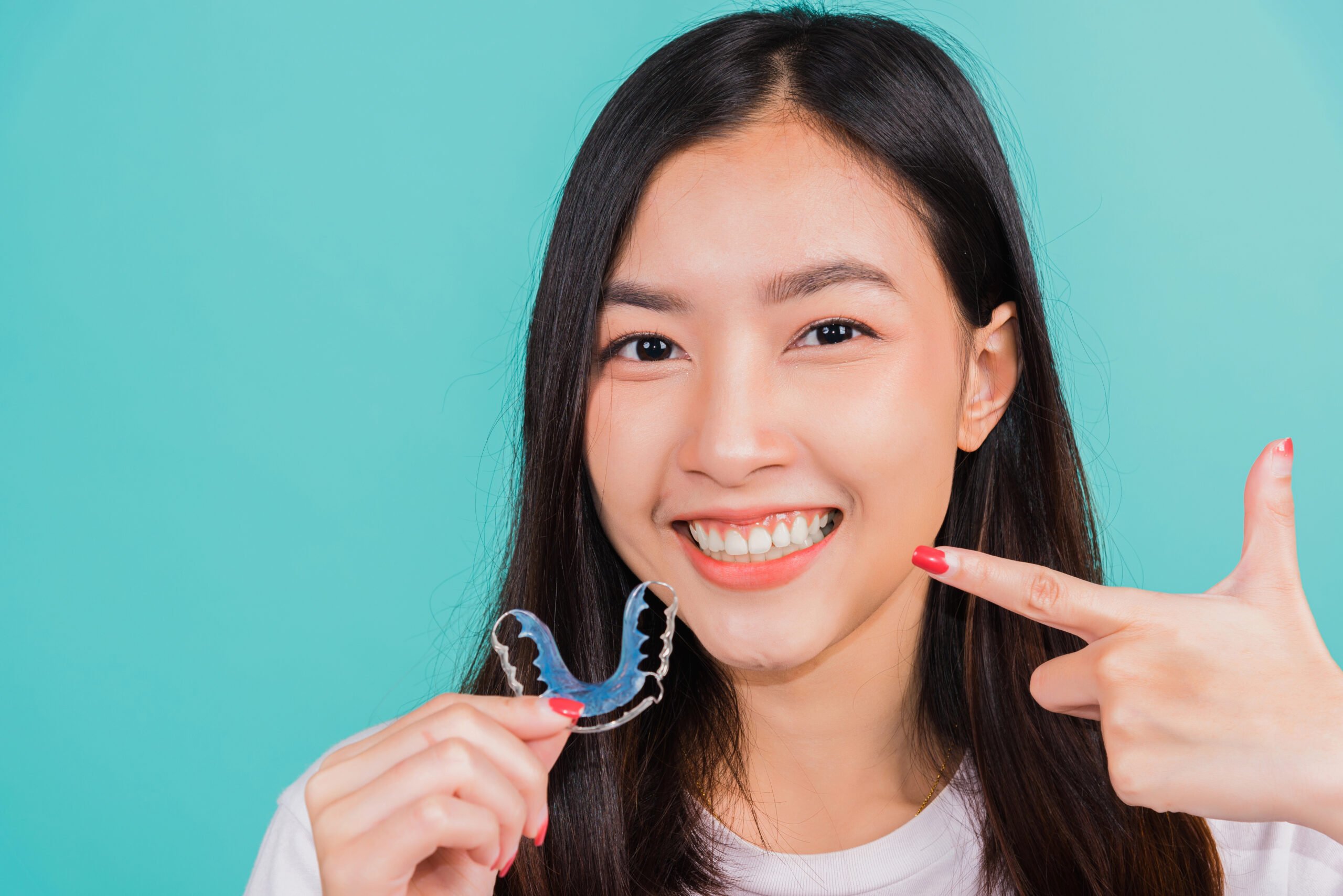 Smiling woman holding retainers to straighten teeth, highlighting an effective orthodontic solution for maintaining a perfectly aligned smile.